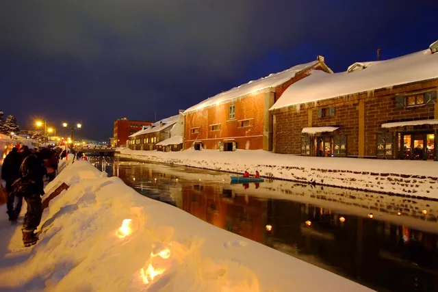 Snow-covered canal-side warehouses in Otaru under fresh falling snow, with gas lamps along the towpath
